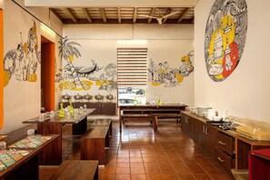 A restaurant with wooden benches, a long dining table, and murals on the walls.