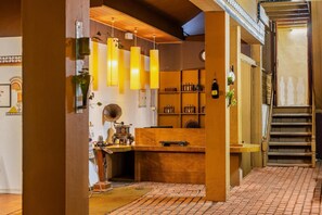 A cozy bar area with hanging lights, shelves with bottles, a wooden counter, and a staircase.
