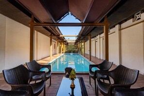 A covered pool area with chairs and a table, a clear view of the pool, and a pergola structure.