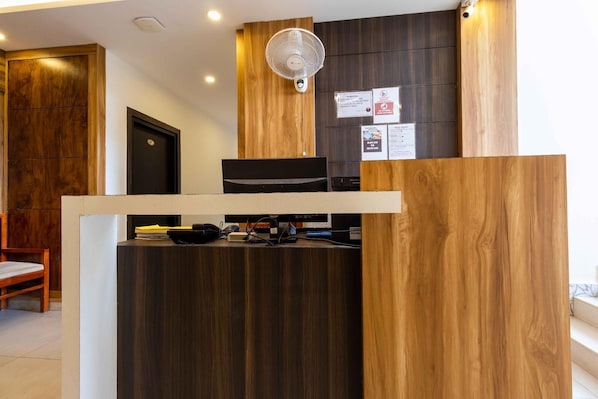 A reception desk with a wooden finish, a wall-mounted fan, and a door. - Hotel Abooz (Bengaluru)
