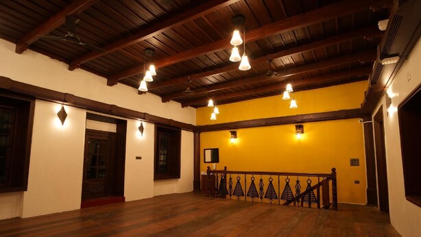 A spacious room with wooden flooring, a high ceiling with exposed beams, and hanging light fixtures. - The Sunset Bay (Kochi)