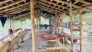 Een overdekt buitengebied met een tafel, stoelen en boekenkasten.