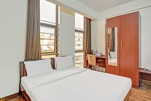 Una habitación de hotel con cama, escritorio, silla, armario y ventanas amplias.
