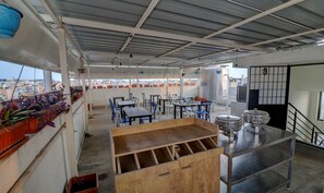 Una terraza en la azotea con mesas, sillas y plantas en macetas.