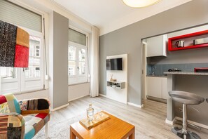 Een moderne woonkamer met een bank, een salontafel, een televisie en een keukenhoek met een rode plank.