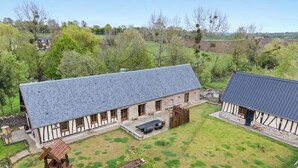 A traditional half-timbered building with a sloped roof, a stone foundation, and a fenced yard. - Gîtes de France® - Hygge (SAUMONT LA POTERIE)