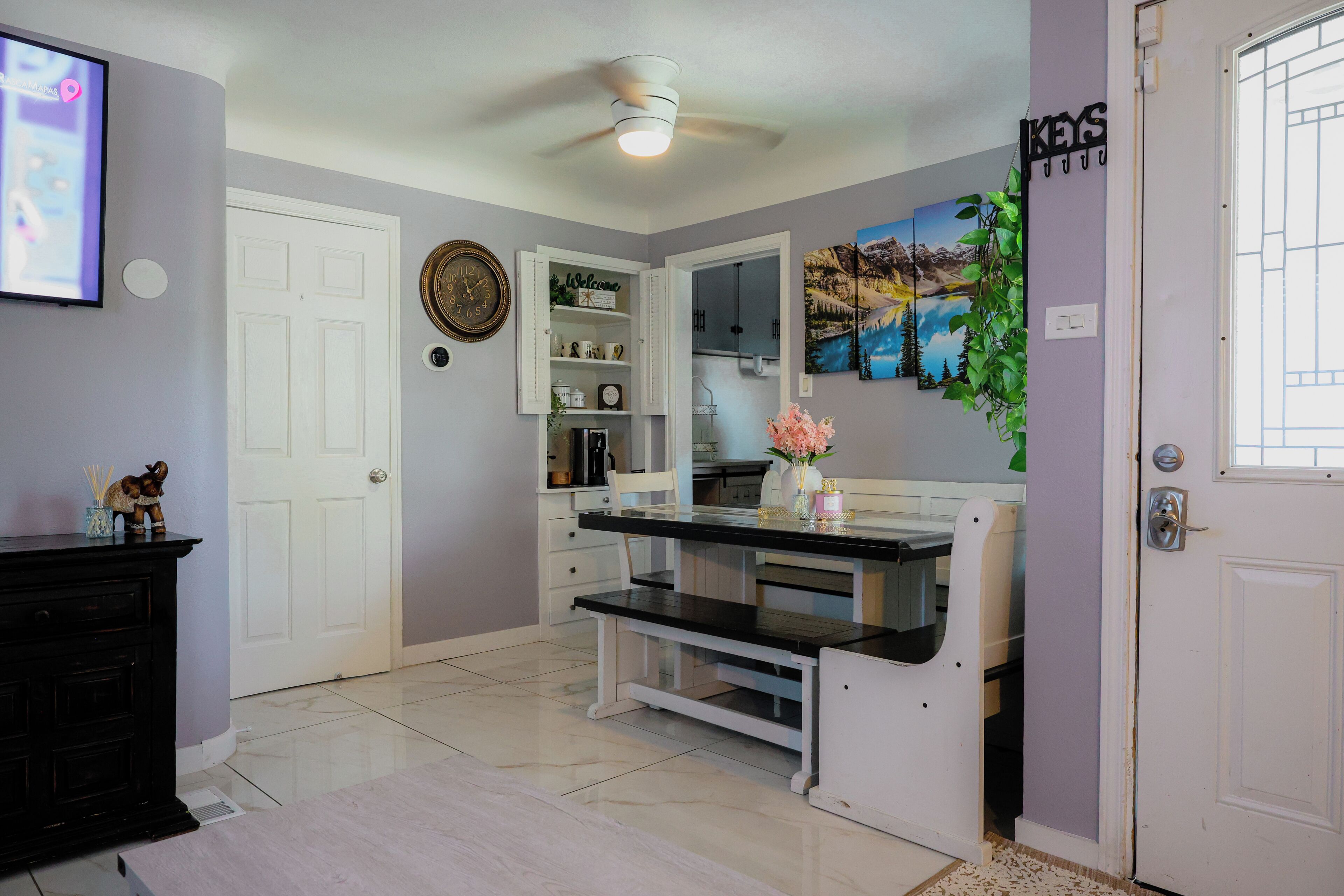A room with a white door, a white bench, a white cabinet, a ceiling fan, and a painting on the wall.