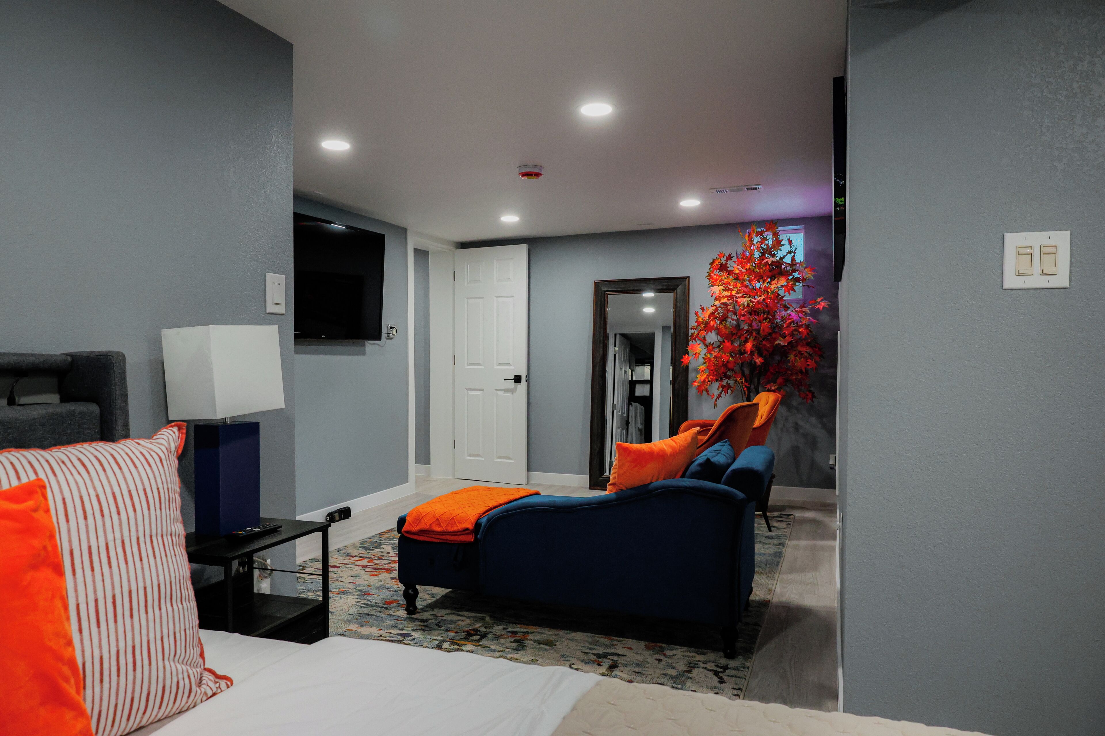 A hotel room with a bed, a desk with a lamp, a TV, a chair, and a large window with a view.