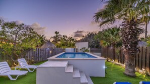Un giardino sul retro con piscina, un pontile di legno e una costruzione con tetto di paglia.