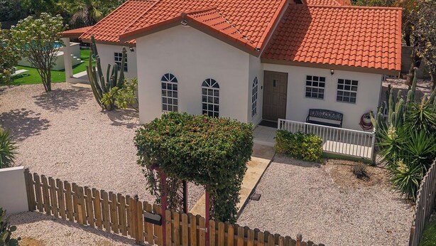 Un edificio a un piano con tetto in tegole rosse, un piccolo portico e un vialetto sterrato.