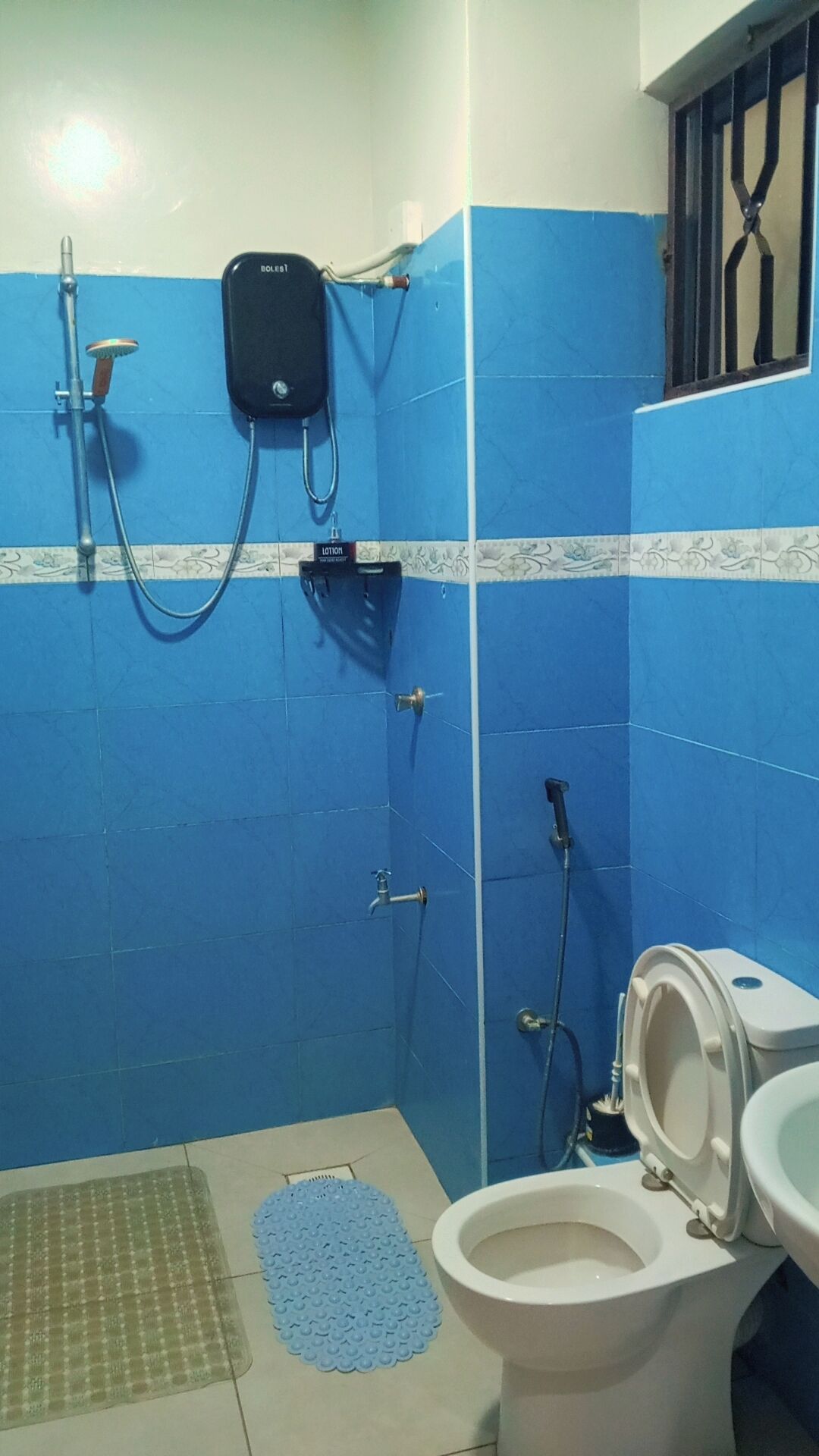 A bathroom with blue tiles, a toilet, a shower with a handheld showerhead, and a soap dispenser.