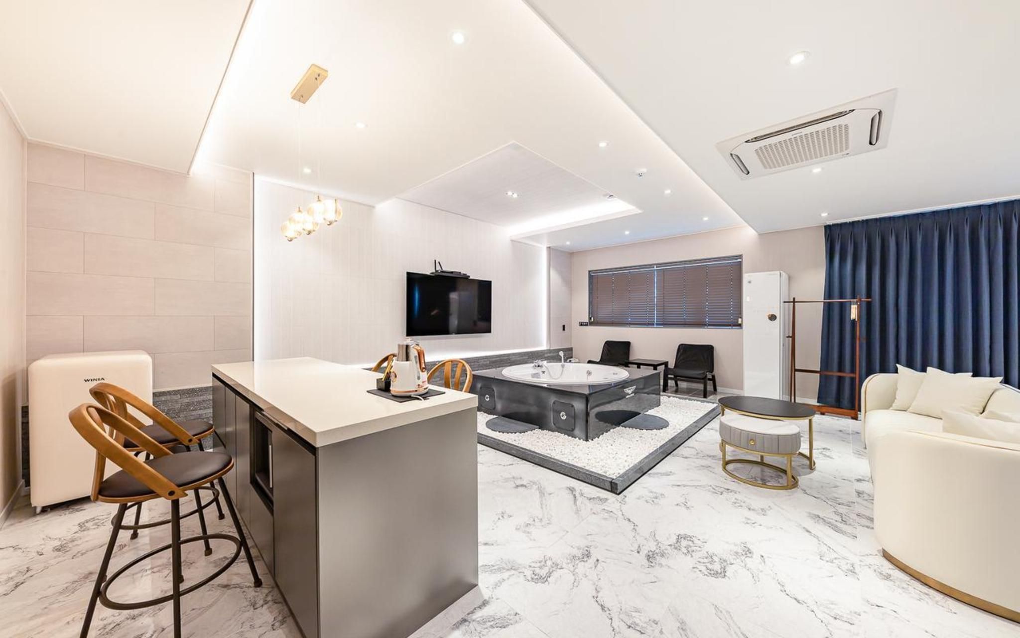 A modern living room with a kitchen area, a large TV, a seating area with a sofa and chairs, and a small round table.
