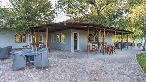 Un patio techado con mobiliario exterior, piso de ladrillo y un edificio con ventanas y una puerta.
