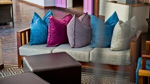 A modern living room with a grey sofa, multiple cushions, a wooden coffee table, and a patterned rug. - Damara Mopane Lodge (Khorixas)