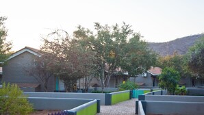 A paved pathway leading to a building with a tiled roof, surrounded by greenery and a hilly landscape. - Damara Mopane Lodge (Khorixas)