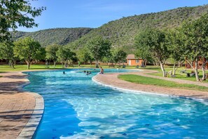 Una piscina con agua azul cristalina, rodeada de árboles y un paisaje montañoso.
