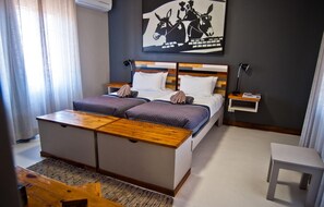 Una habitación de hotel con cama, mesitas de noche, un escritorio y una obra de arte colgada en la pared.