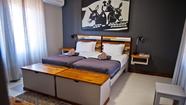 A hotel room with a bed, bedside tables, a desk, and a wall-mounted artwork. - Damara Mopane Lodge (Khorixas)