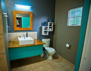 Un baño con tocador de madera, un lavamanos blanco, un inodoro, un espejo y una ventana.