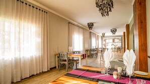 A dining area with wooden tables, chairs, and a long table with a patterned table runner. - Damara Mopane Lodge (Khorixas)