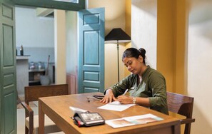 A person seated at a wooden table with a notebook, a pen, and a calculator.