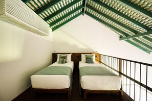 A room with two beds, a wooden headboard, a balcony with a railing, and a sloped ceiling with green beams. - Kayaam House (Rekawa)