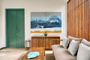 A living room with a green door, a painting, a wooden cabinet, a sofa, and a coffee table. - Kayaam House (Rekawa)