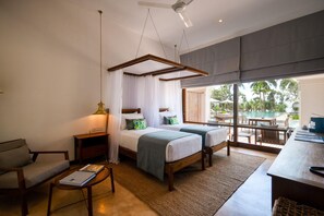 A bedroom with two beds, a nightstand, a chair, a table, and a view of an outdoor pool area. - Kayaam House (Rekawa)