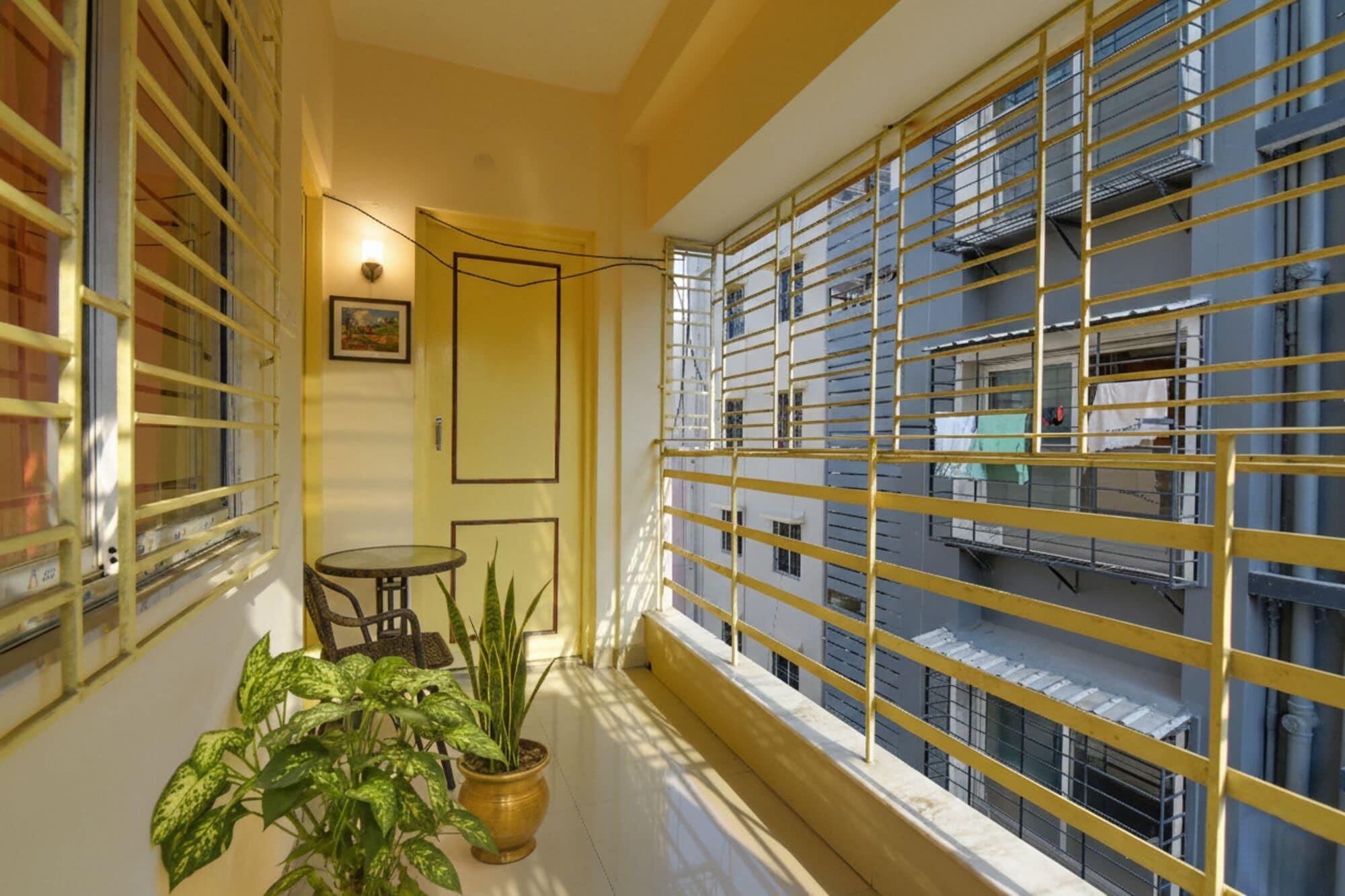 A balcony with yellow metal railings, a potted plant, a small round table, and a chair.