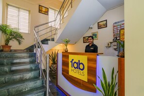 A hotel reception area with a staircase, a receptionist, and a reception desk with a sign. - Collection O 81451 Capital Casa (Barasat)