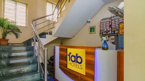 A hotel reception desk with a staircase leading to upper floors, a potted plant, and a security camera. - Collection O 81451 Capital Casa (Barasat)