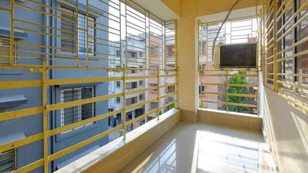 A balcony with yellow metal railings, a view of neighboring buildings, and a small air conditioning unit on the wall. - Collection O 81451 Capital Casa (Barasat)