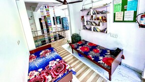 Quarto com duas camas, um ventilador de teto, uma estante de livros e um mural de avisos.