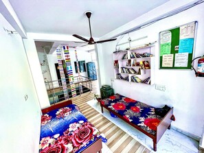 Een kamer met twee bedden, een plafondventilator, een boekenkast en een prikbord.