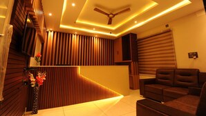 A modern interior with a wooden reception desk, a ceiling fan, and a seating area with a large window. - Mc Suites Mysuru (Mysore)