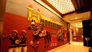 A hotel lobby with a mural of traditional figures, a geometric ceiling design, and a reception area with a vase of flowers. - Mc Suites Mysuru (Mysore)