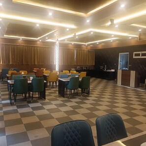A dining area with checkered flooring, multiple tables, and chairs. - Mc Suites Mysuru (Mysore)