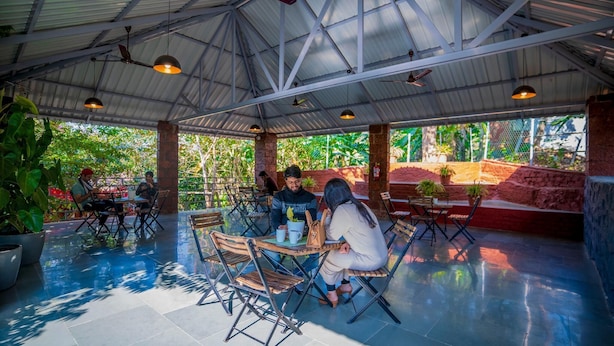 An outdoor cafe with tables and chairs, a metal roof, and potted plants. - Saveda Farm Cottages By Spicy Mango (Karjat)