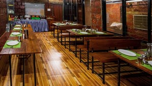 A restaurant with wooden tables and benches, a brick wall, and a large window. - Saveda Farm Cottages By Spicy Mango (Karjat)