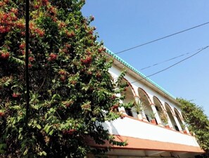 Un edificio con fachada blanca, tejado de tejas rojas y un balcón con macetas.