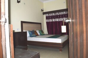 Un dormitorio con cama de madera, una mesita de noche, un tendedero y una lámpara de pared con cortinas.