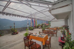 A covered outdoor seating area with tables and chairs, potted plants, and a view of mountains. - Palri Boutique Hotel (Gangtok)