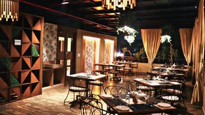 A restaurant with tables and chairs, hanging lights, and a patterned wall. - Hotel Rion (Udaipur)