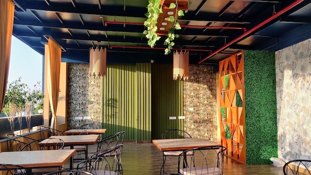 An outdoor seating area with tables and chairs, a green wall with a vertical garden, and a patterned wall. - Hotel Rion (Udaipur)