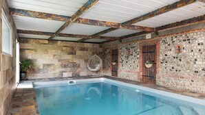 A swimming pool with stone walls and a hanging chair. - Gîtes de France® - L'Orée D'Etretat (LA POTERIE CAP D'ANTIFER)