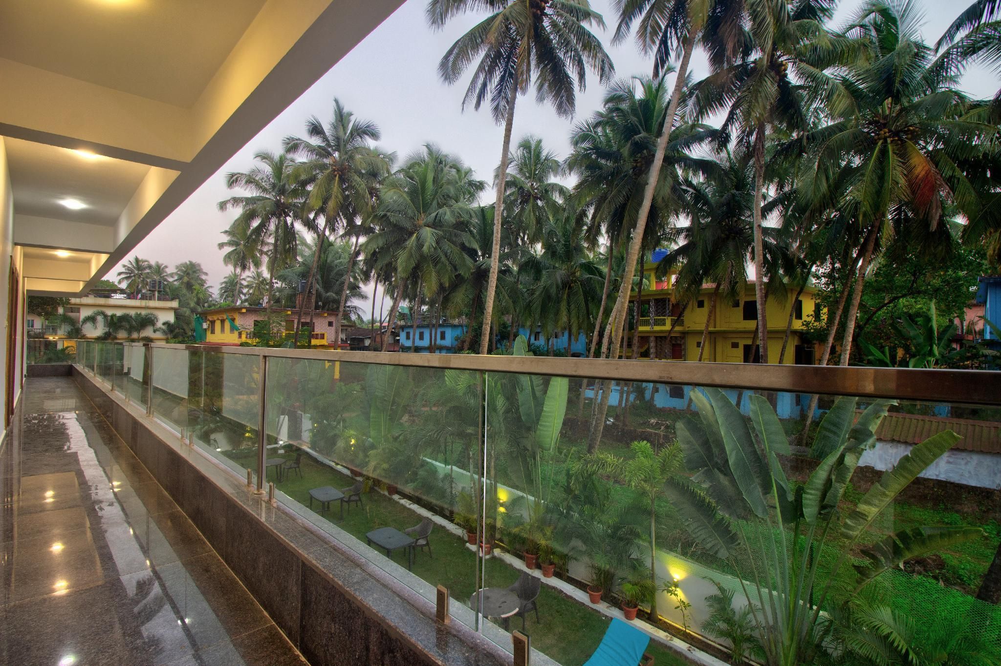 A balcony with a glass railing overlooking a garden with palm trees and a pool.