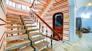 A grand staircase with marble steps and a wooden handrail, leading to a red door. - Fabexpress The Dove (Guwahati)