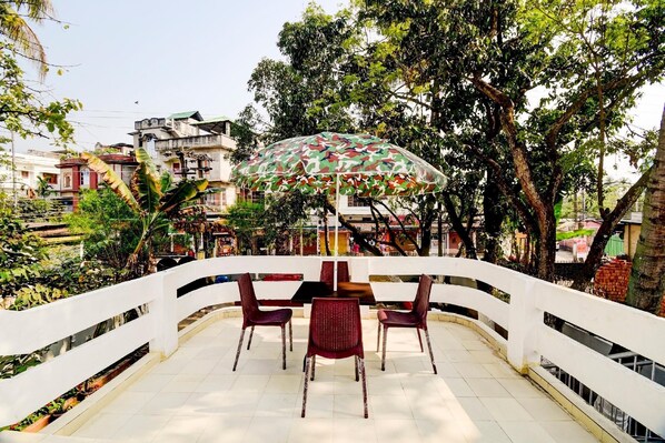 A terrace with a table and chairs, an umbrella, and a white railing. - Fabexpress The Dove (Guwahati)