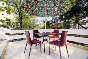 An outdoor seating area with a table and chairs, an umbrella, and a view of buildings and trees. - Fabexpress The Dove (Guwahati)