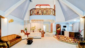 A spacious living area with a high ceiling, a balcony with a railing, and a reception desk. - Fabexpress The Dove (Guwahati)